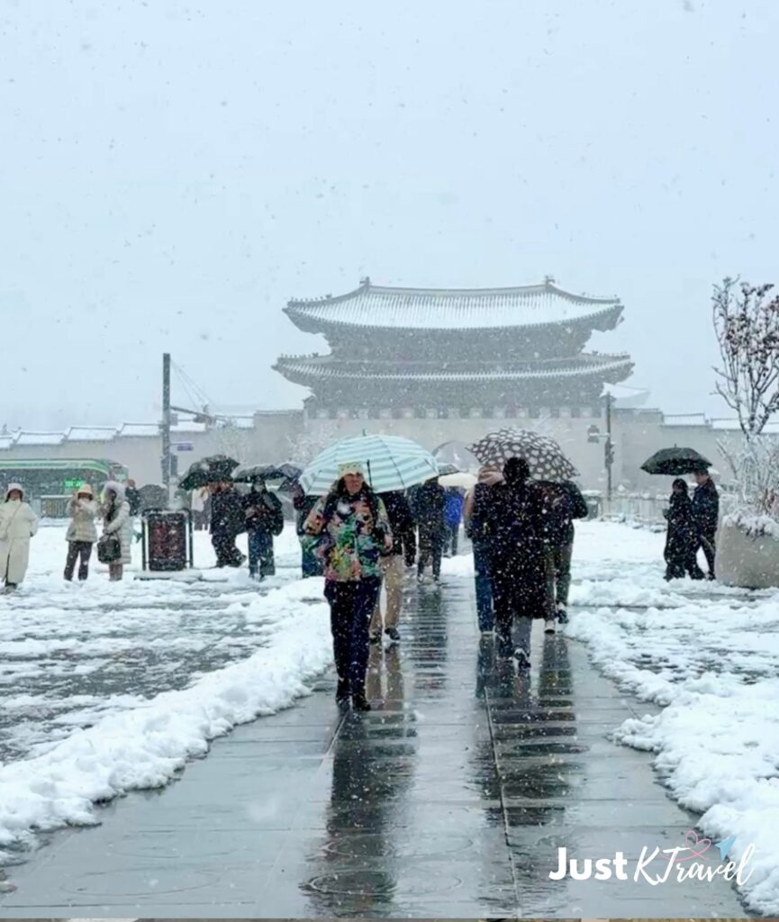 People with umbrellas walking near Gwanghwamun Gate during heavy snowfall in Seoul